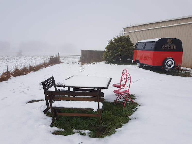 image of a picnic table and the Small Acres Cyder Kombi trailer covered in snow; winter cellar door