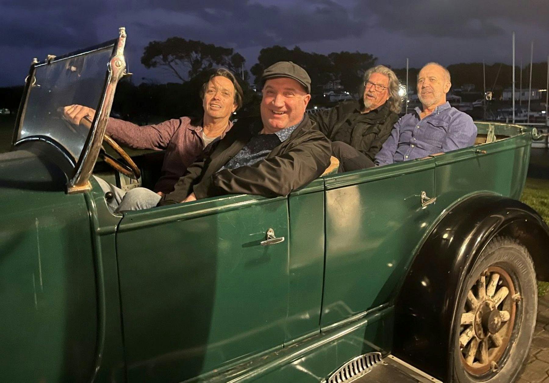 Four band members in a green vintage car