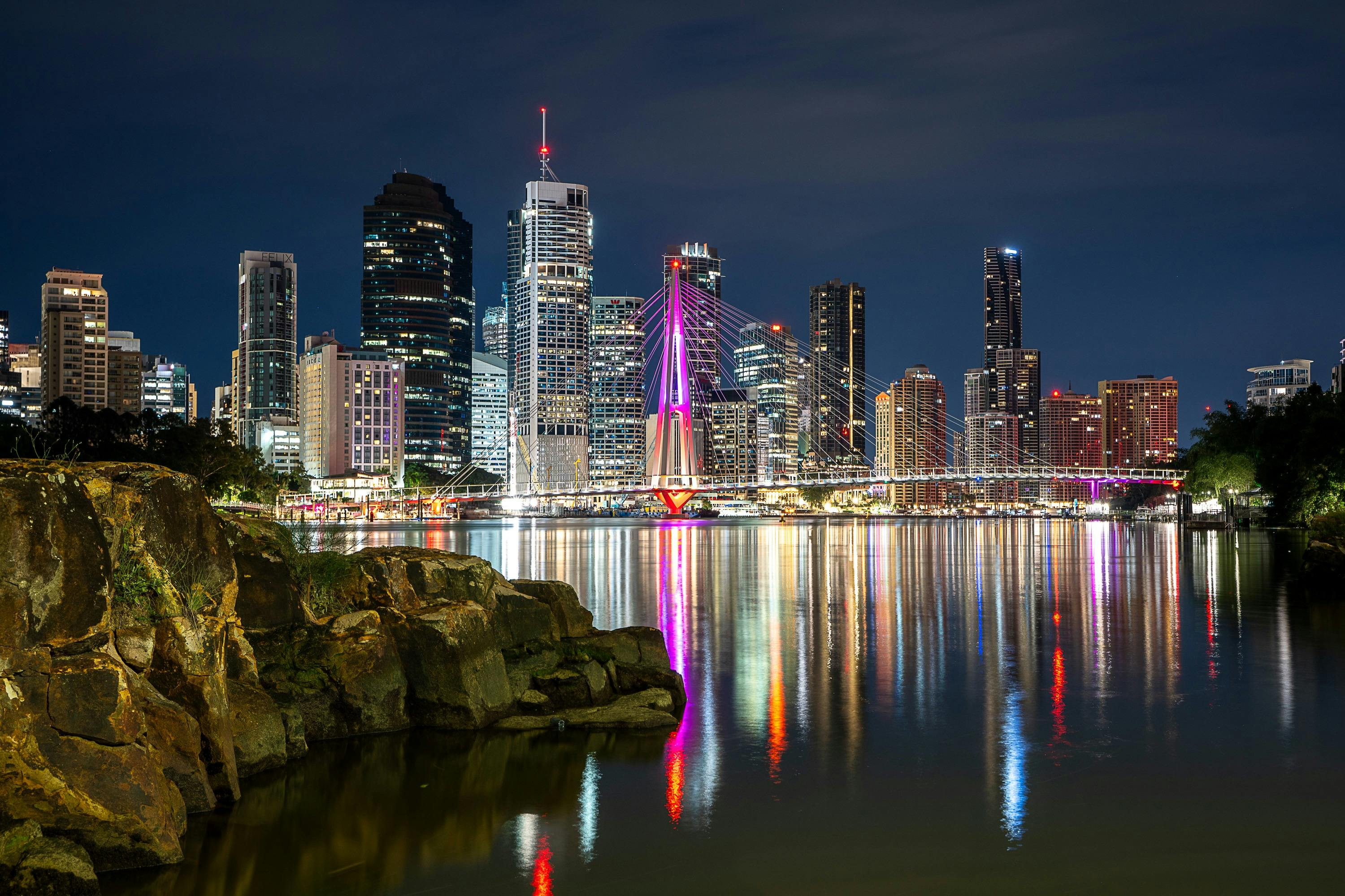 Picture of Brisbane City at night with the Story Bridge, river and rocks showing.