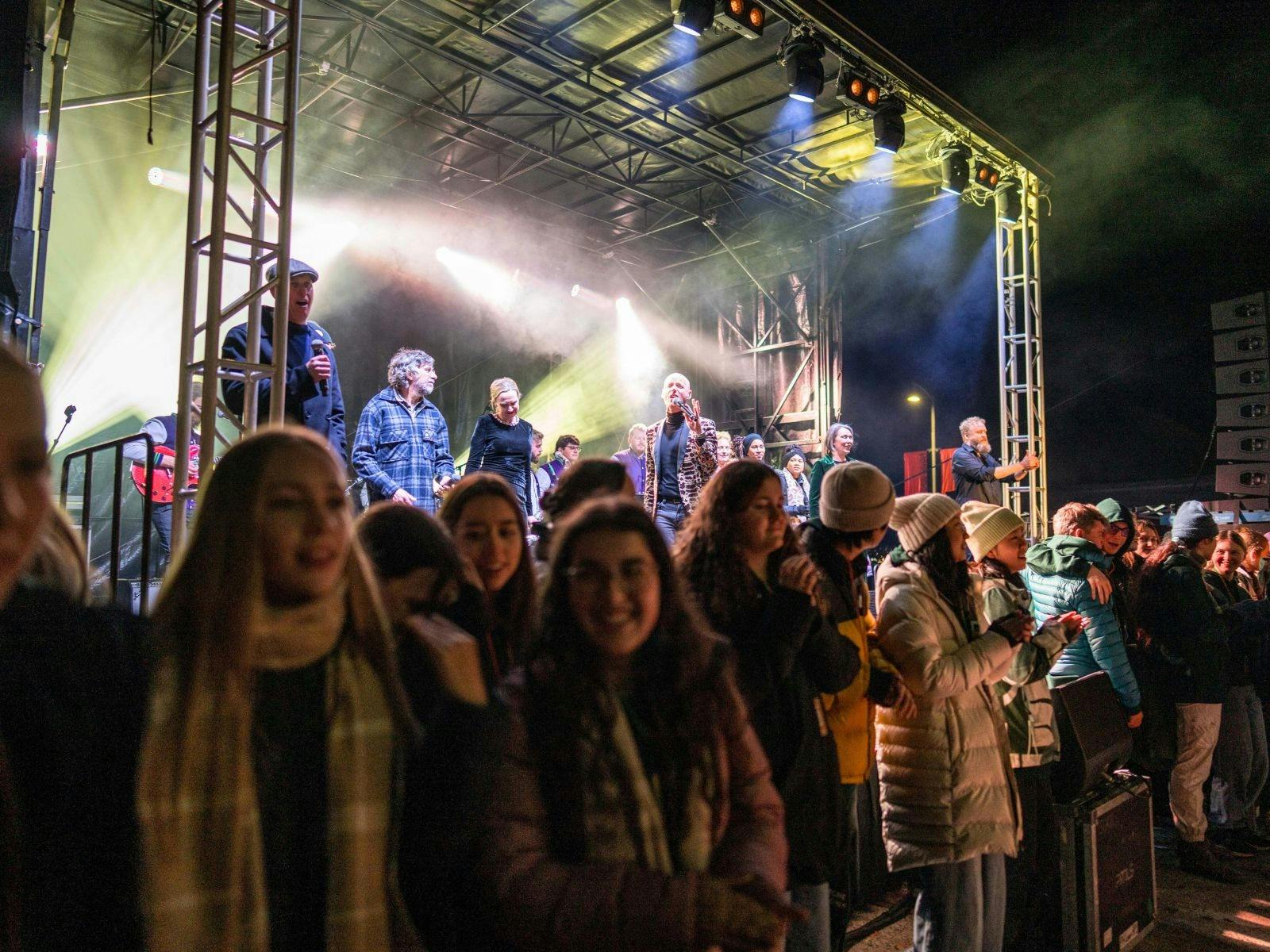 Crowd watching an outdoor night concert with bright lights and a metal stage structure