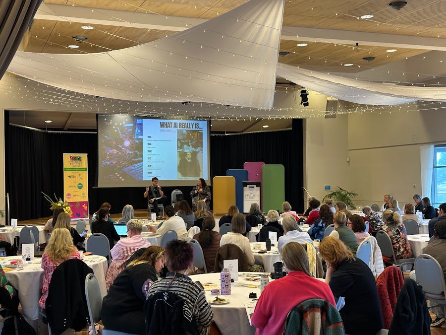 A full auditorium of 80 people listening to a talk on stage. Bright airy room.