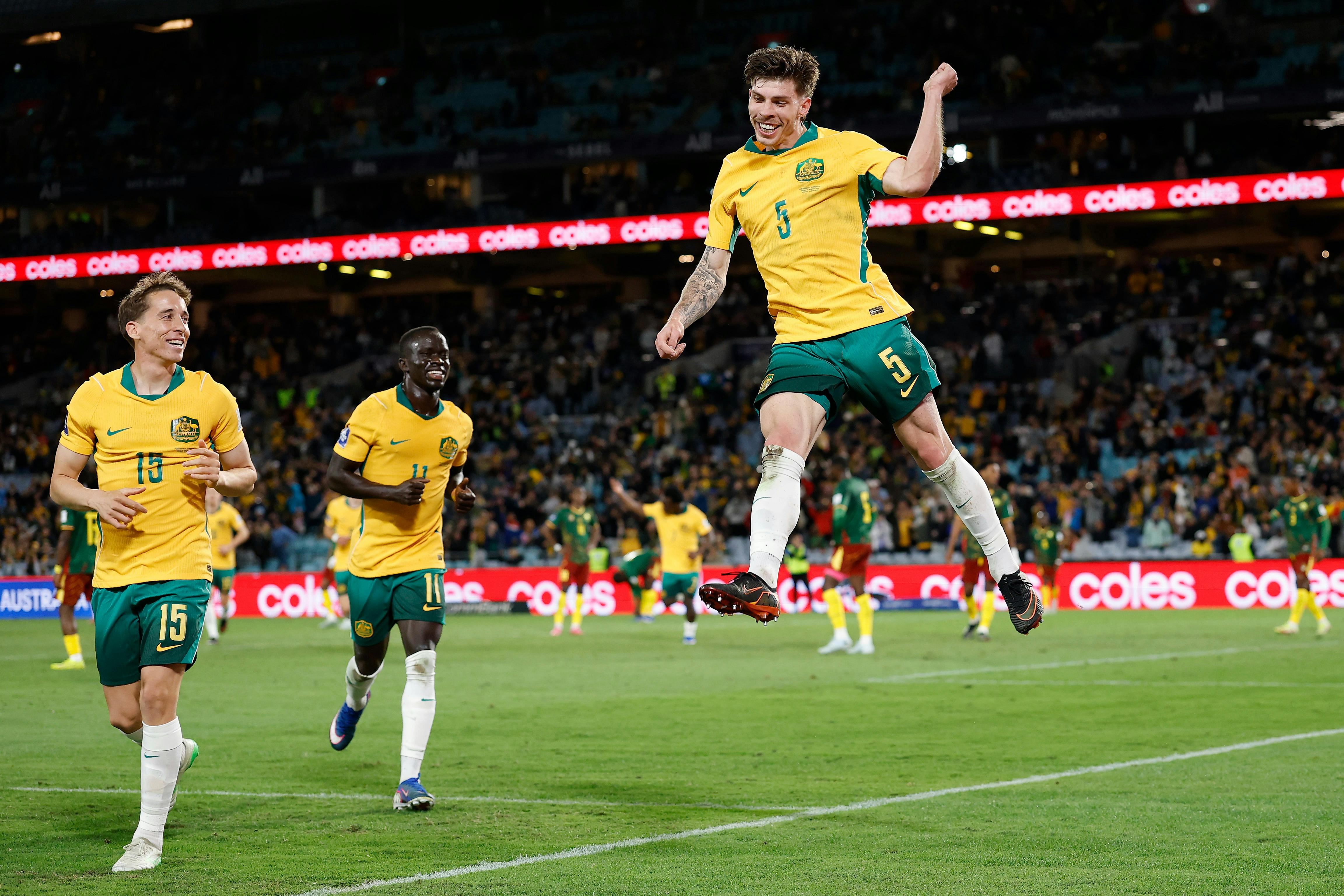 Soccer players in yellow kits celebrate a goal on a stadium pitch as teammates run in behind