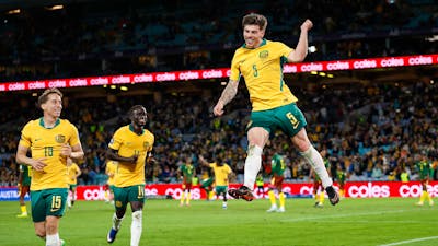 Soccer players in yellow kits celebrate a goal on a stadium pitch as teammates run in behind