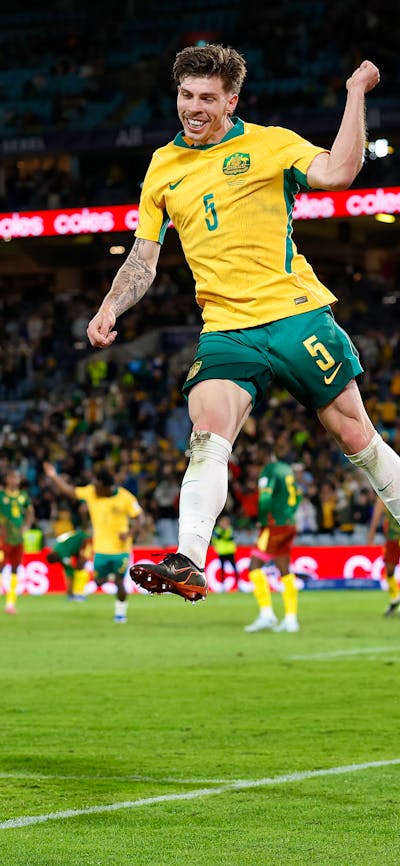 Soccer players in yellow kits celebrate a goal on a stadium pitch as teammates run in behind