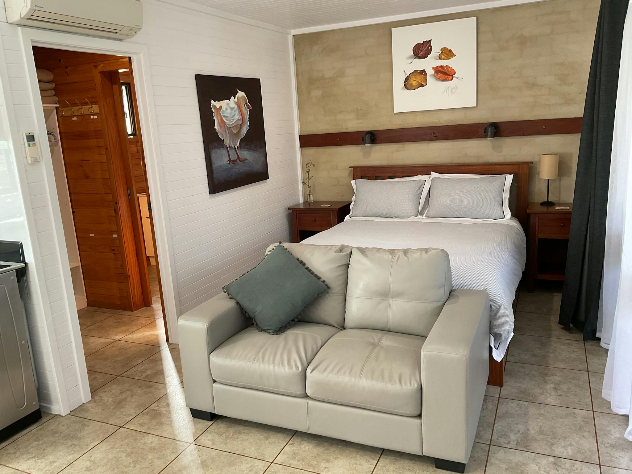 A made up guest room with a queen bed, sofa and art on the walls.
