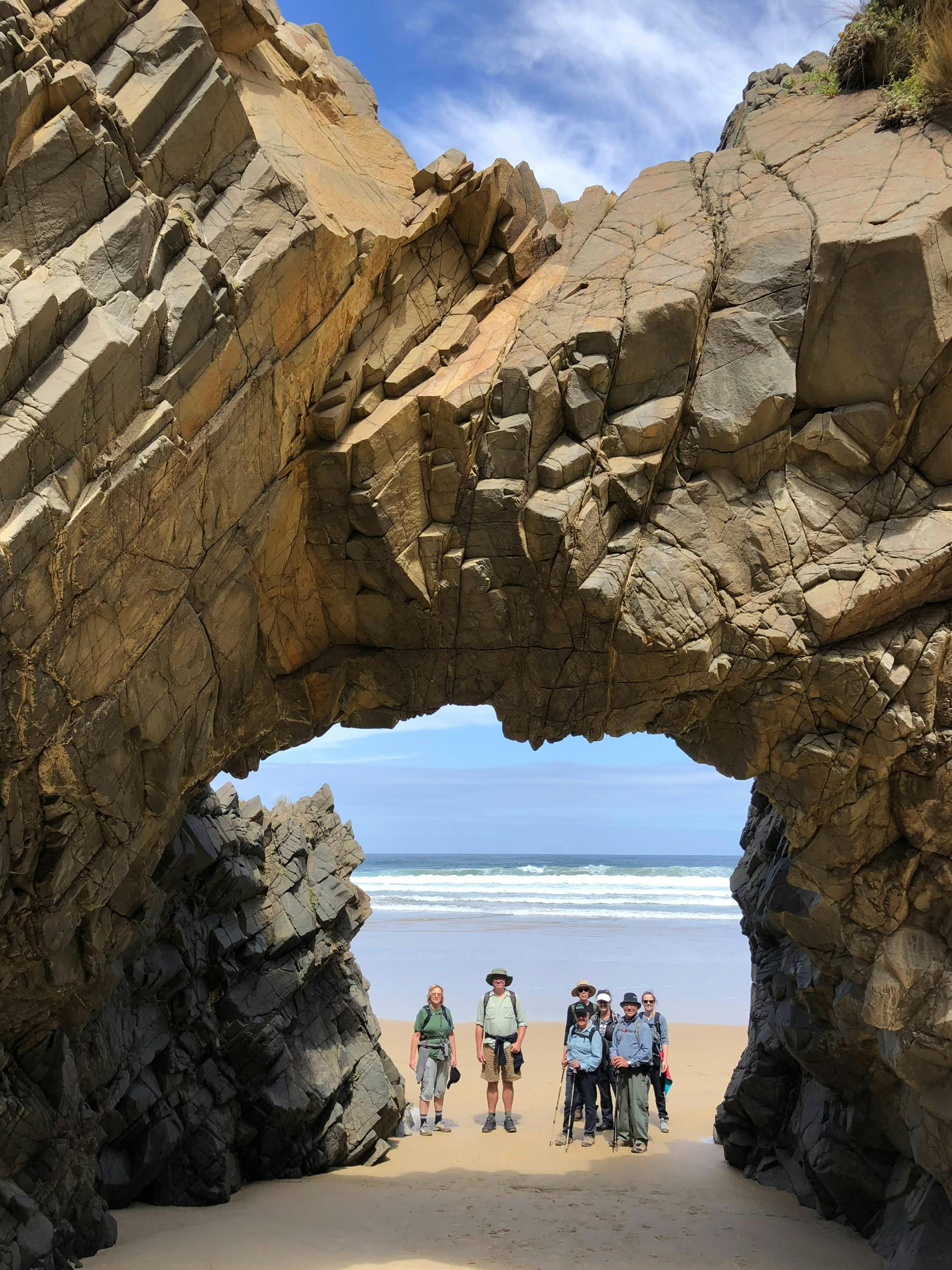 Group standing under a large rock arch on a beach on Bruny Island Tasmania.
