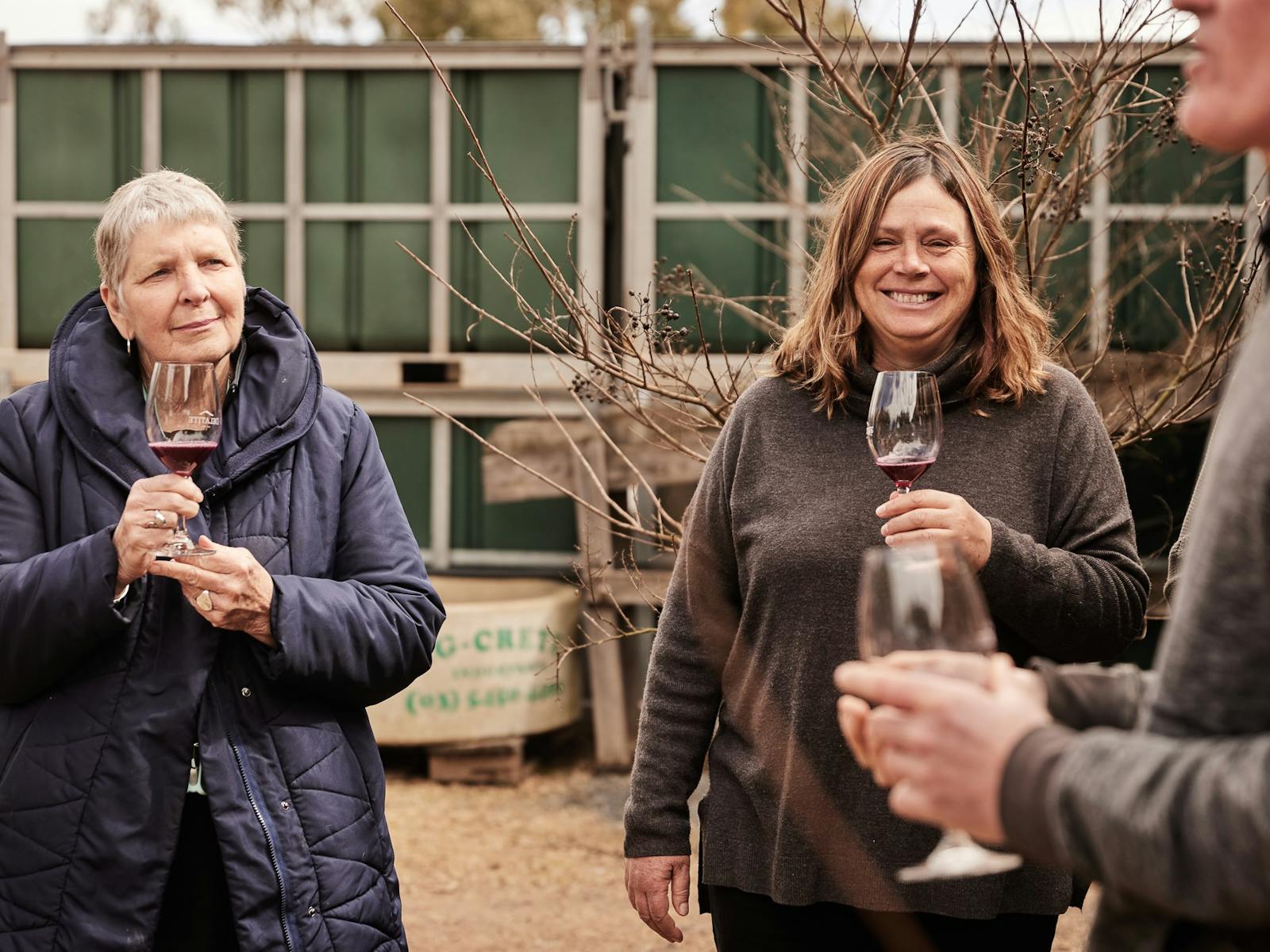 Three people standing outside holding wine glasses