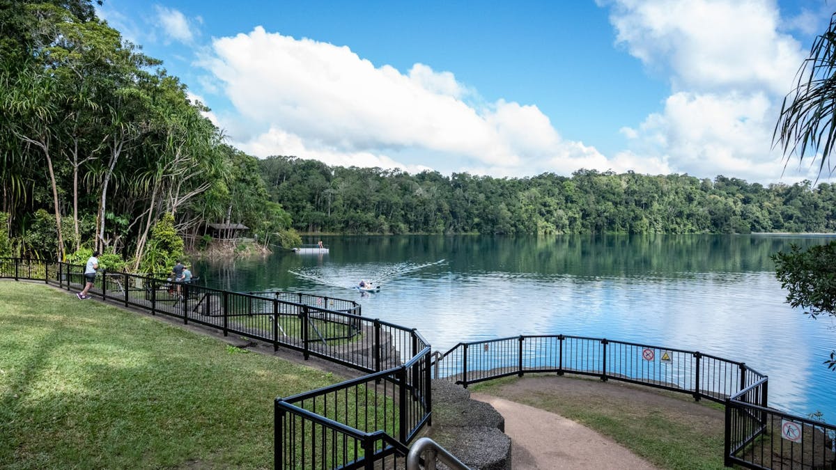 Fence around lake where people are kayaking and on the pontoon in the distance.