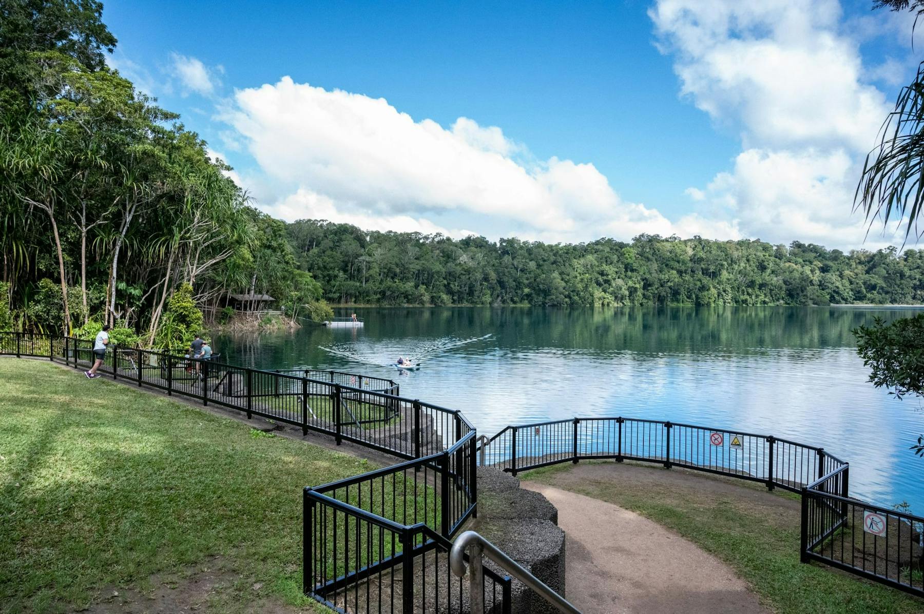 Fence around lake where people are kayaking and on the pontoon in the distance.