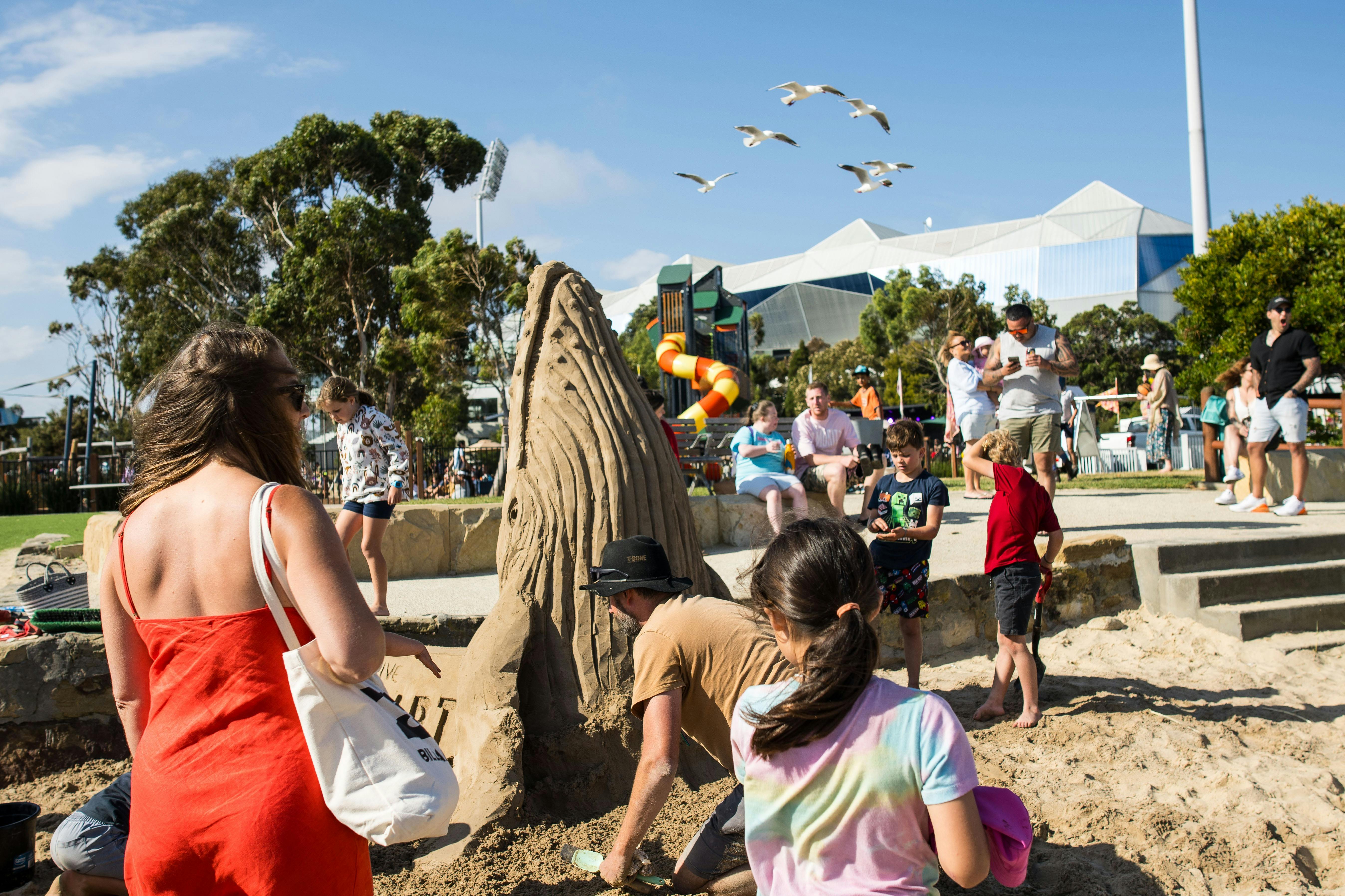 Crowds of people stand on a beach admiring a large sand sculpture of a whale.