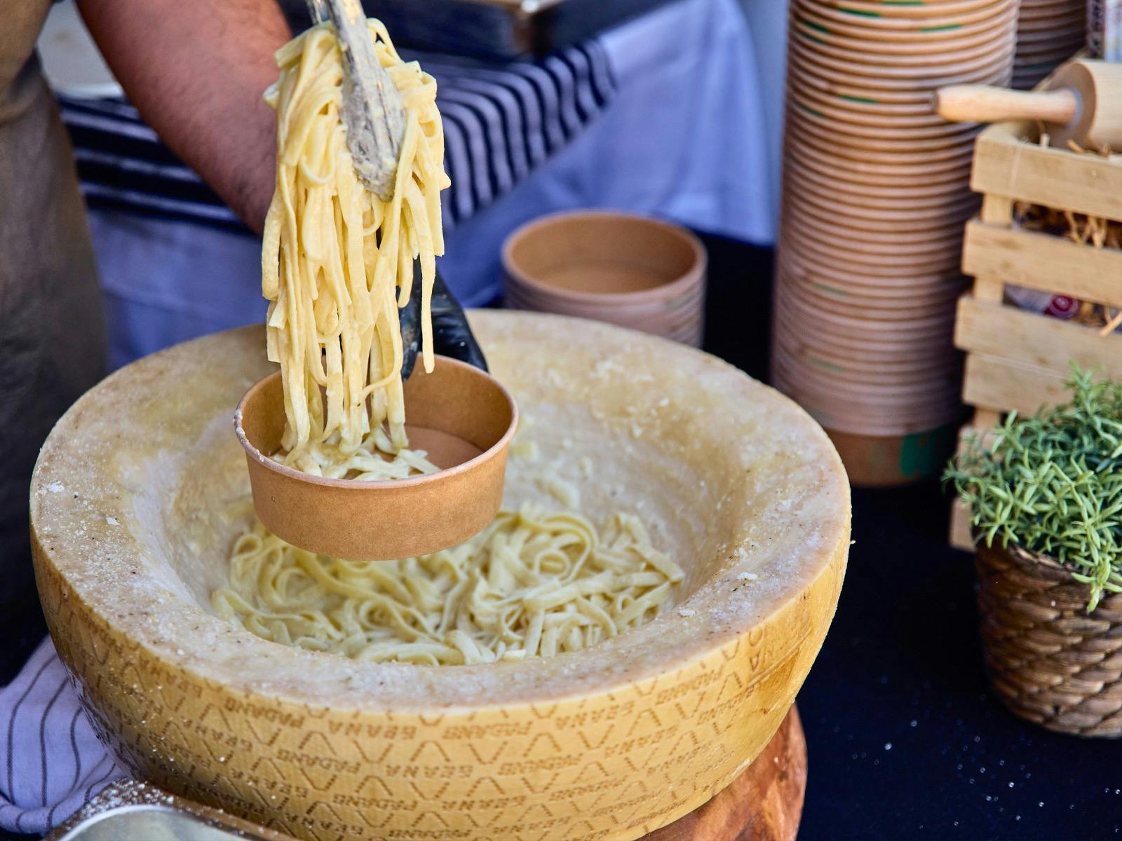 Tongs placing freshly cooked cacio e Pepe into a bowl above a parmesan wheel