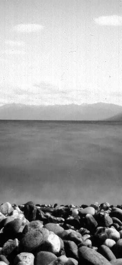 A black and white image of a rocky beach and water surrounded by mountains