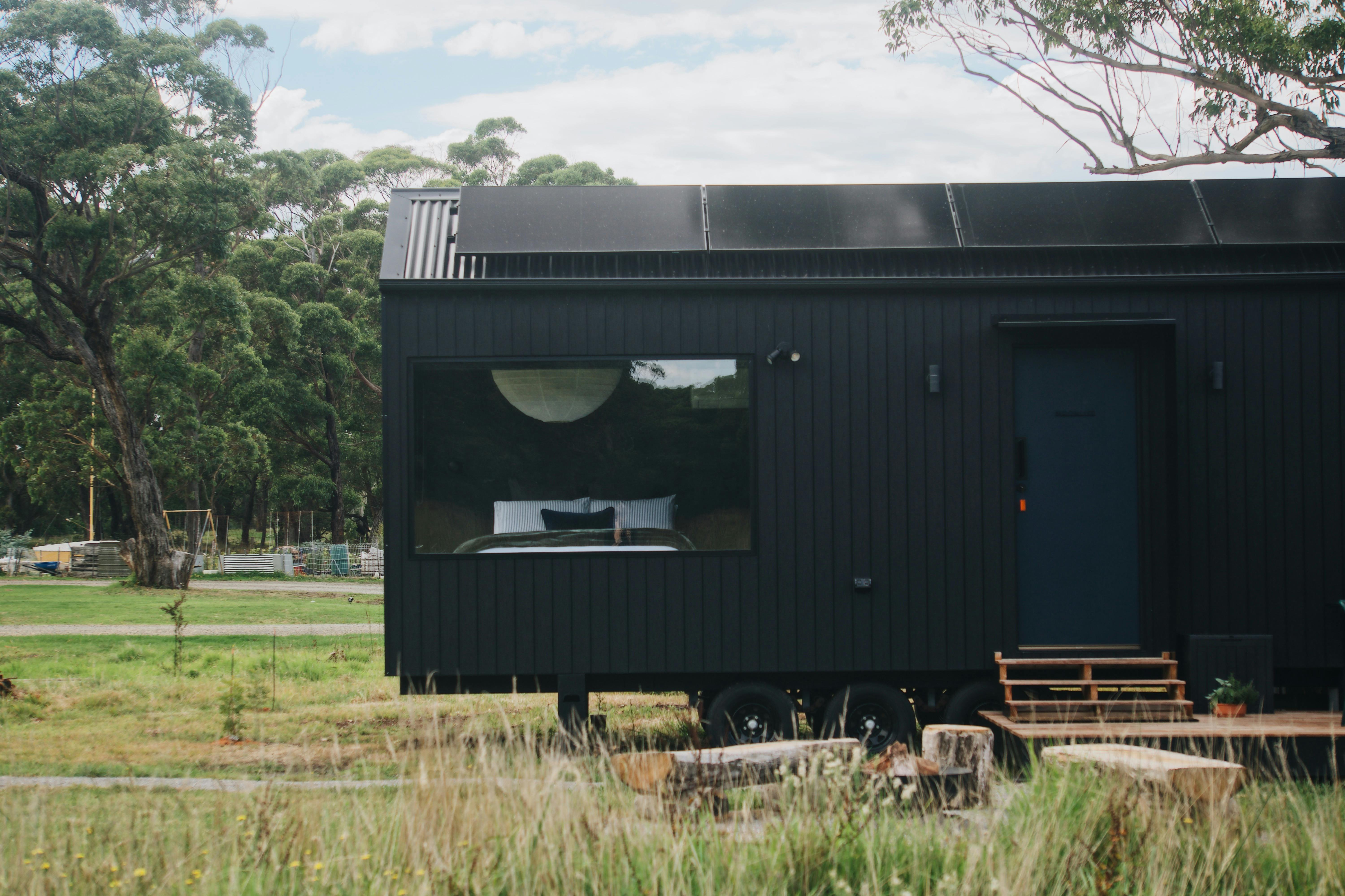 A black tiny home stands alone in a clearing