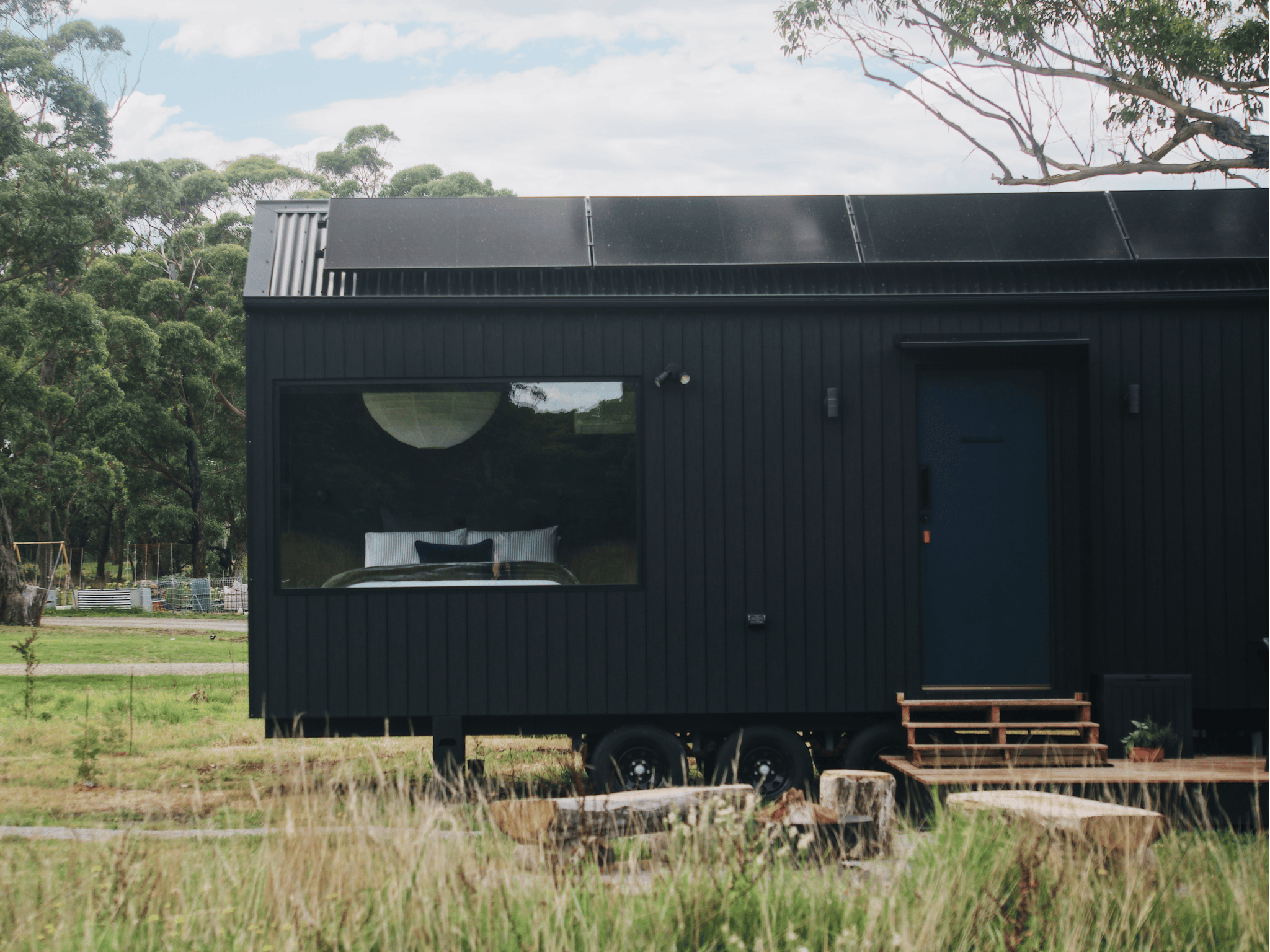 A black tiny home stands alone in a clearing