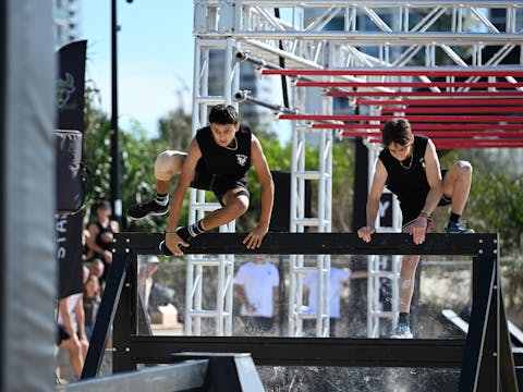 Two male athletes scaling a wall obstacle
