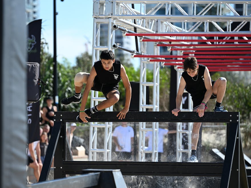 Two male athletes scaling a wall obstacle