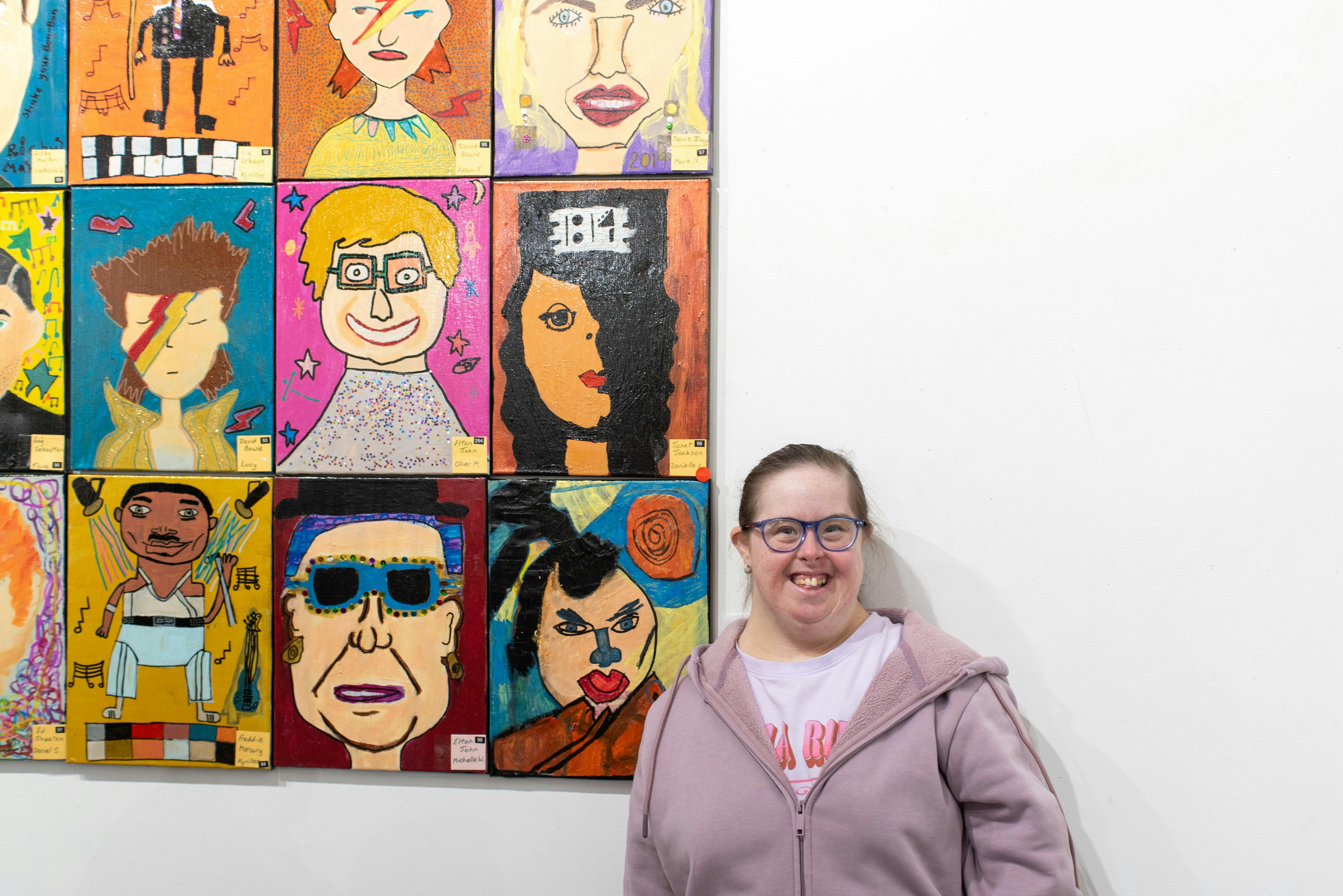 A woman with Down syndrome stands next to a collection of art works