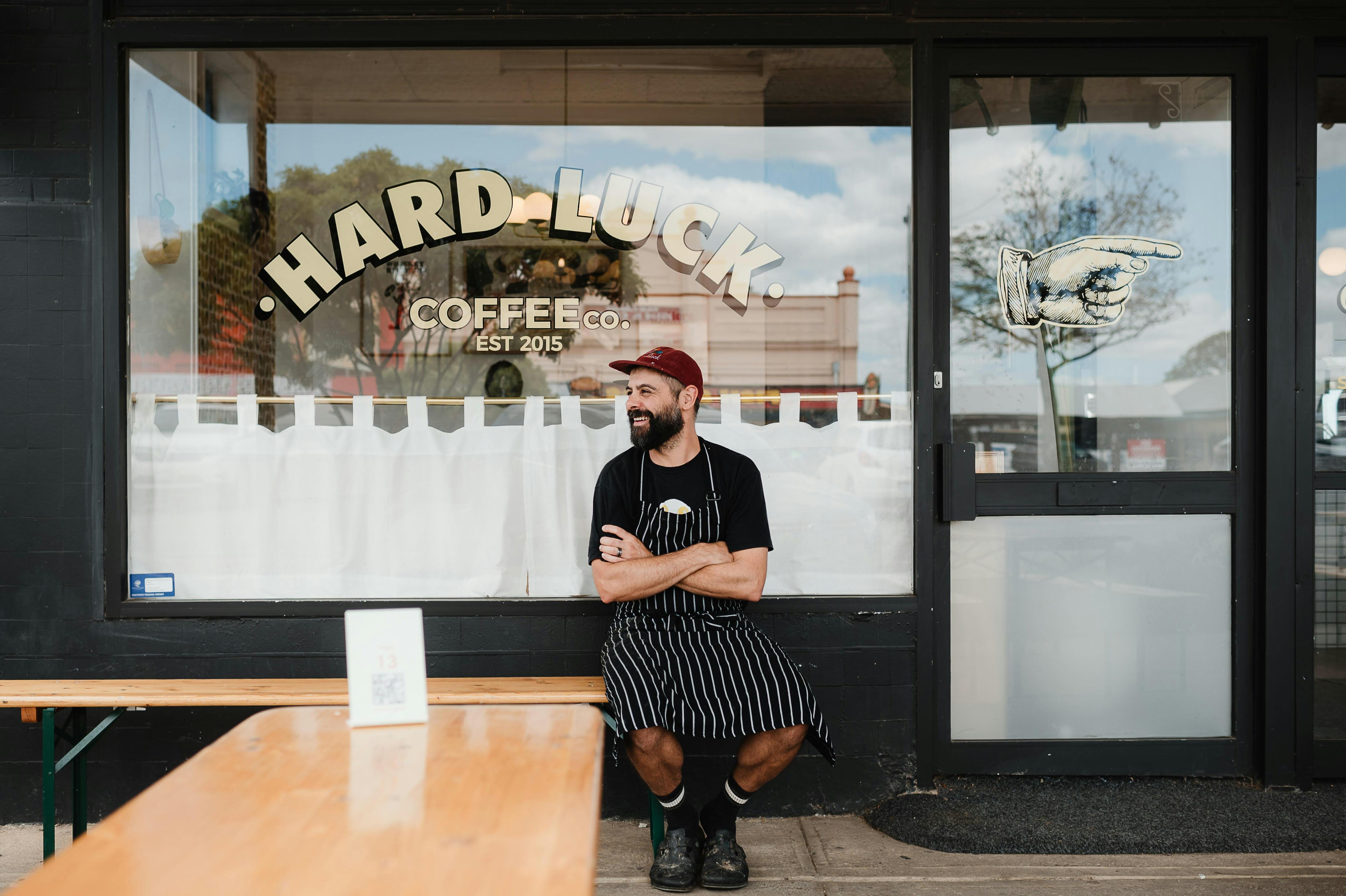 Chef sitting outside shopfront with Hardluck Coffee logo on window