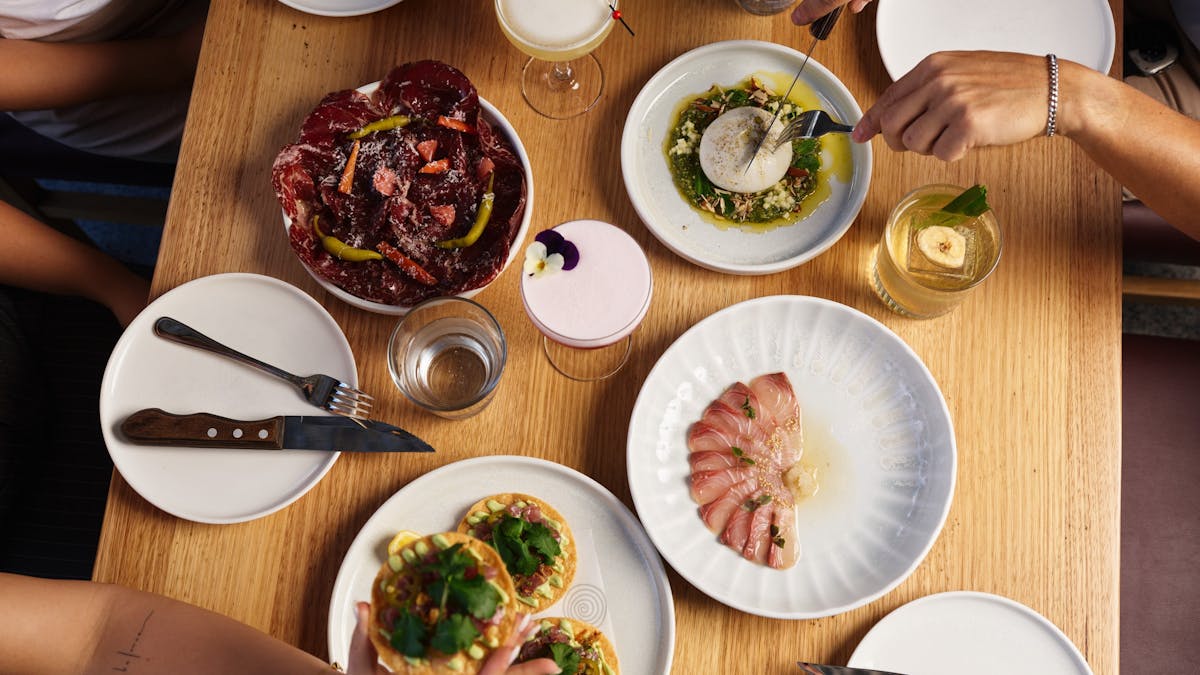 Plates of Hurricane's Surfers Paradise kingfish, tuna tostada, wagyu bresaola & burrata with drinks.
