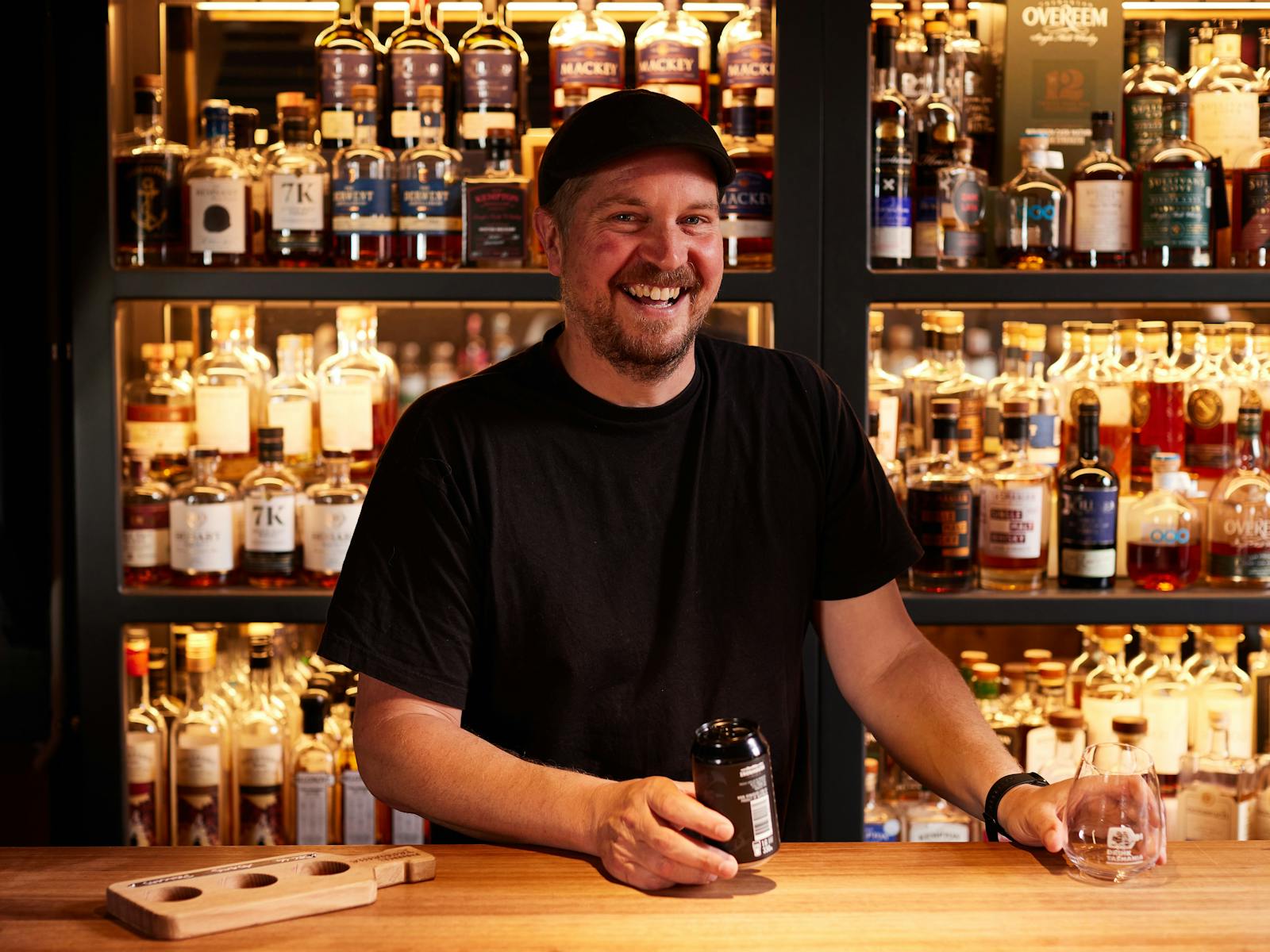 Smiling staff member about to pour a drink with shelves of delicious spirits behind them.