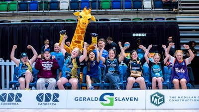 A group of young UC Capitals fans cheering while sitting courtside in a row.
