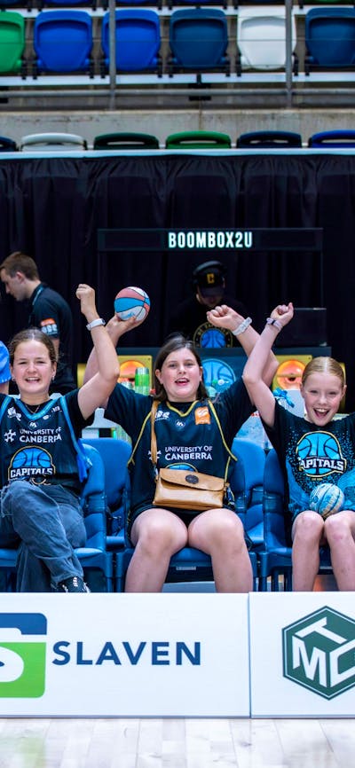 A group of young UC Capitals fans cheering while sitting courtside in a row.