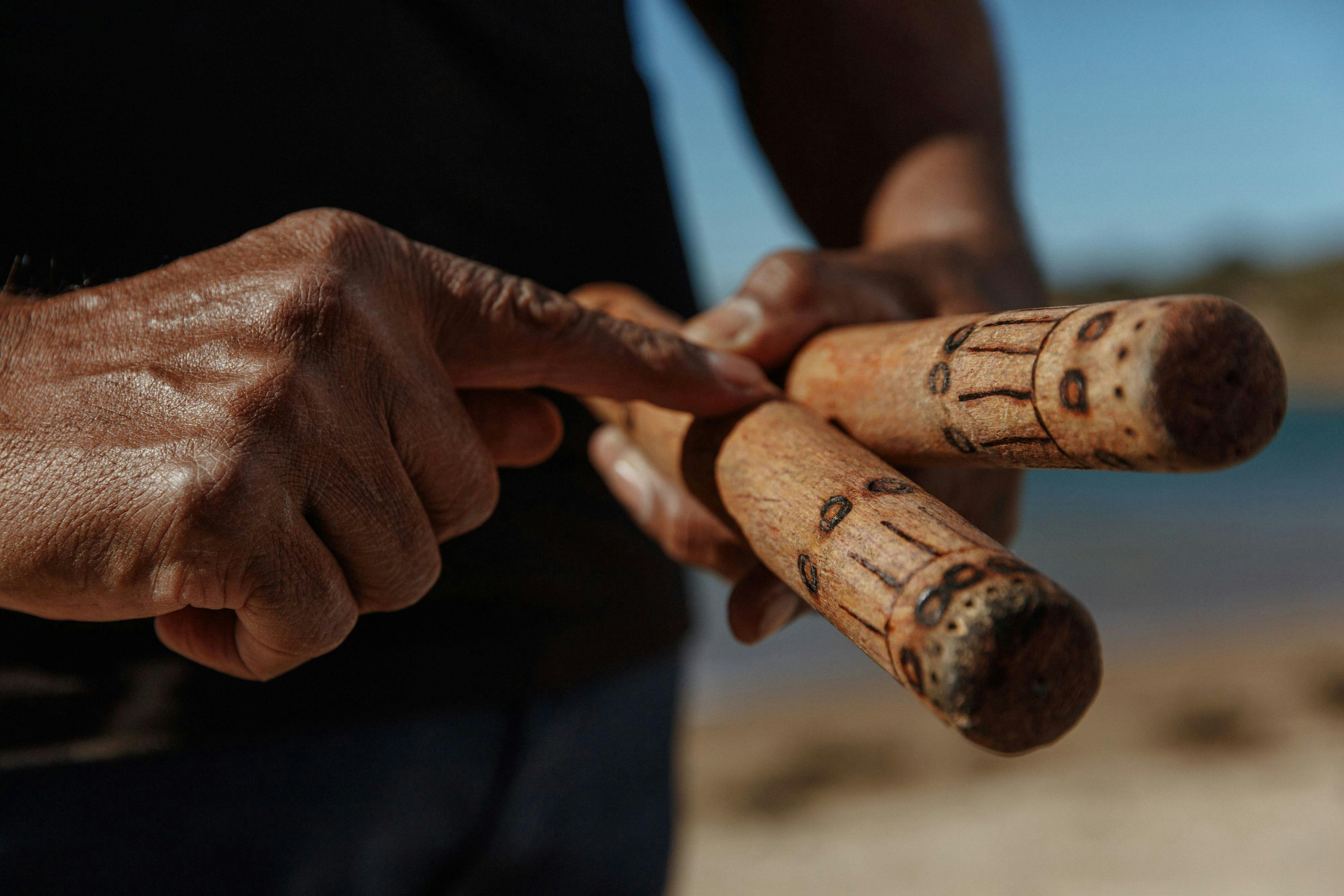 a man holding two wooden sticks pointing at the artwork