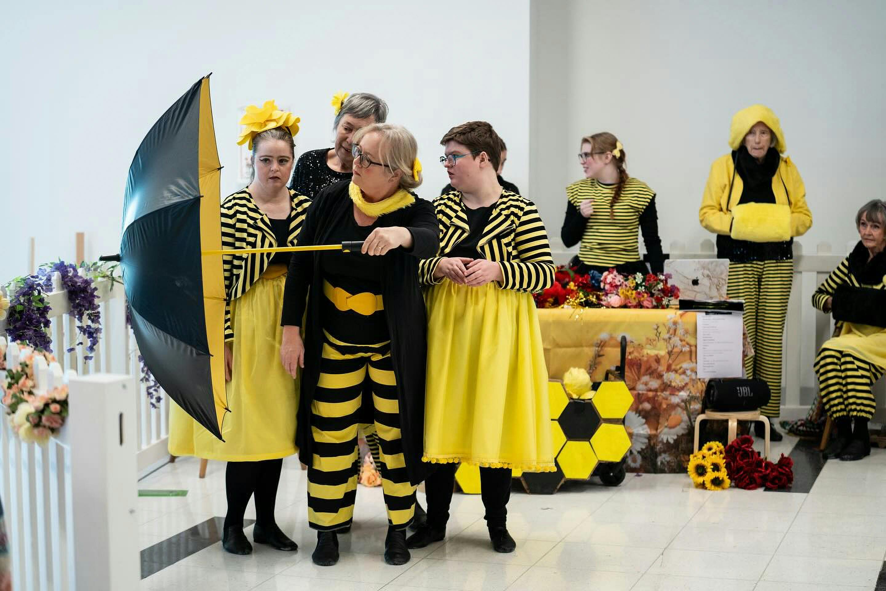 A group of dancers dressed in yellow and black reminiscent of bees perform with umbrella