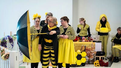 A group of dancers dressed in yellow and black reminiscent of bees perform with umbrella