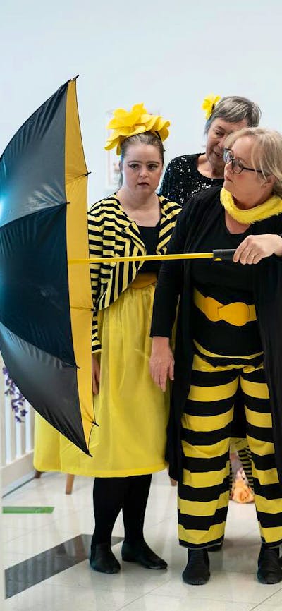 A group of dancers dressed in yellow and black reminiscent of bees perform with umbrella