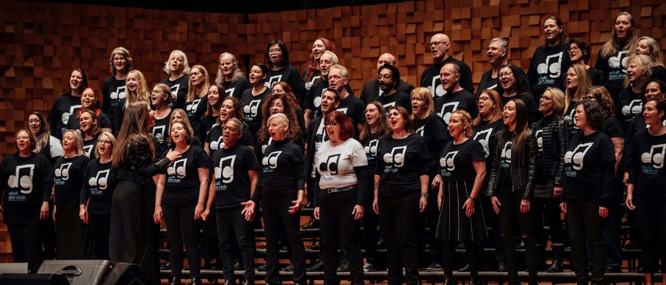 A group of singers wearing black tops with white music notes on them sing on stage
