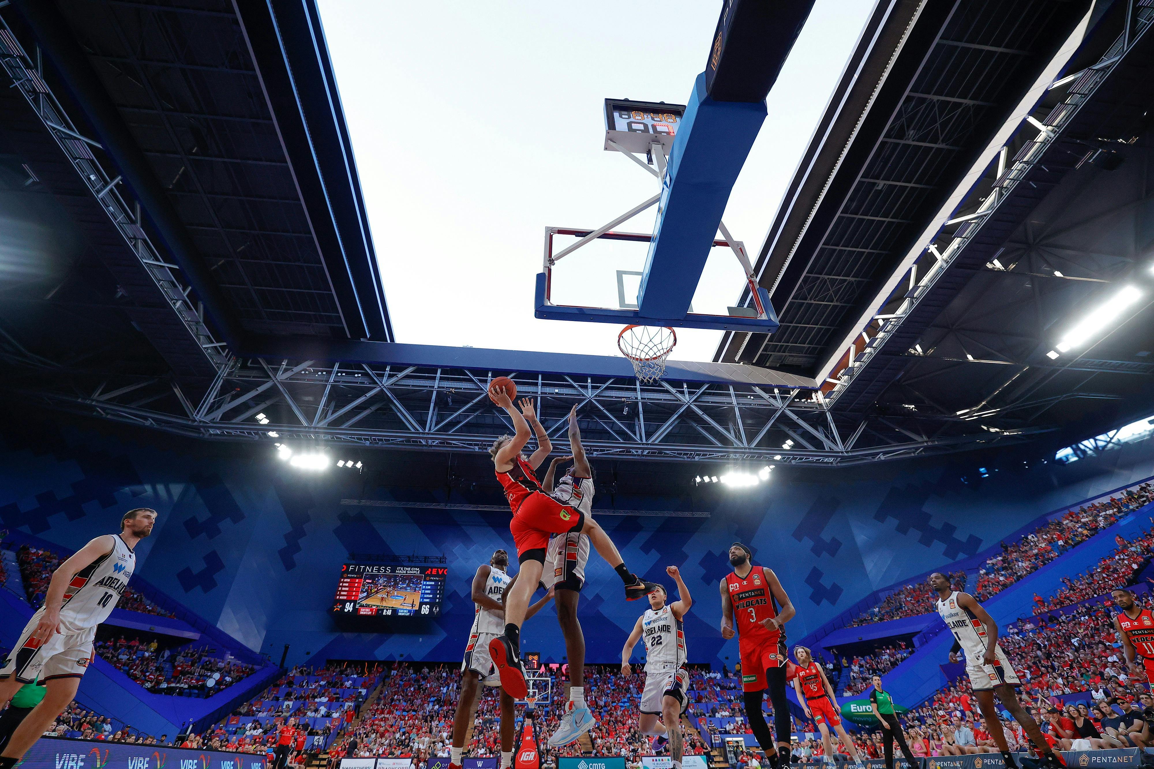 A basketball player jumps towards the hoop whilst another defends at RAC Arena with the roof open