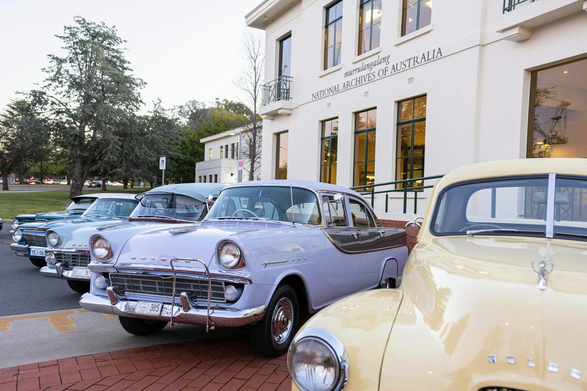 Photograph of pastel coloured classic Holden cars parked on display in front of NAA canberra