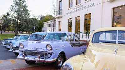 Photograph of pastel coloured classic Holden cars parked on display in front of NAA canberra