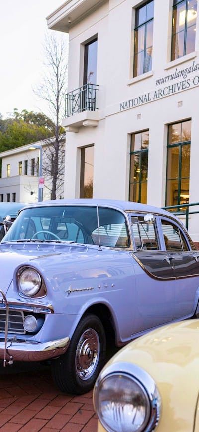 Photograph of pastel coloured classic Holden cars parked on display in front of NAA canberra