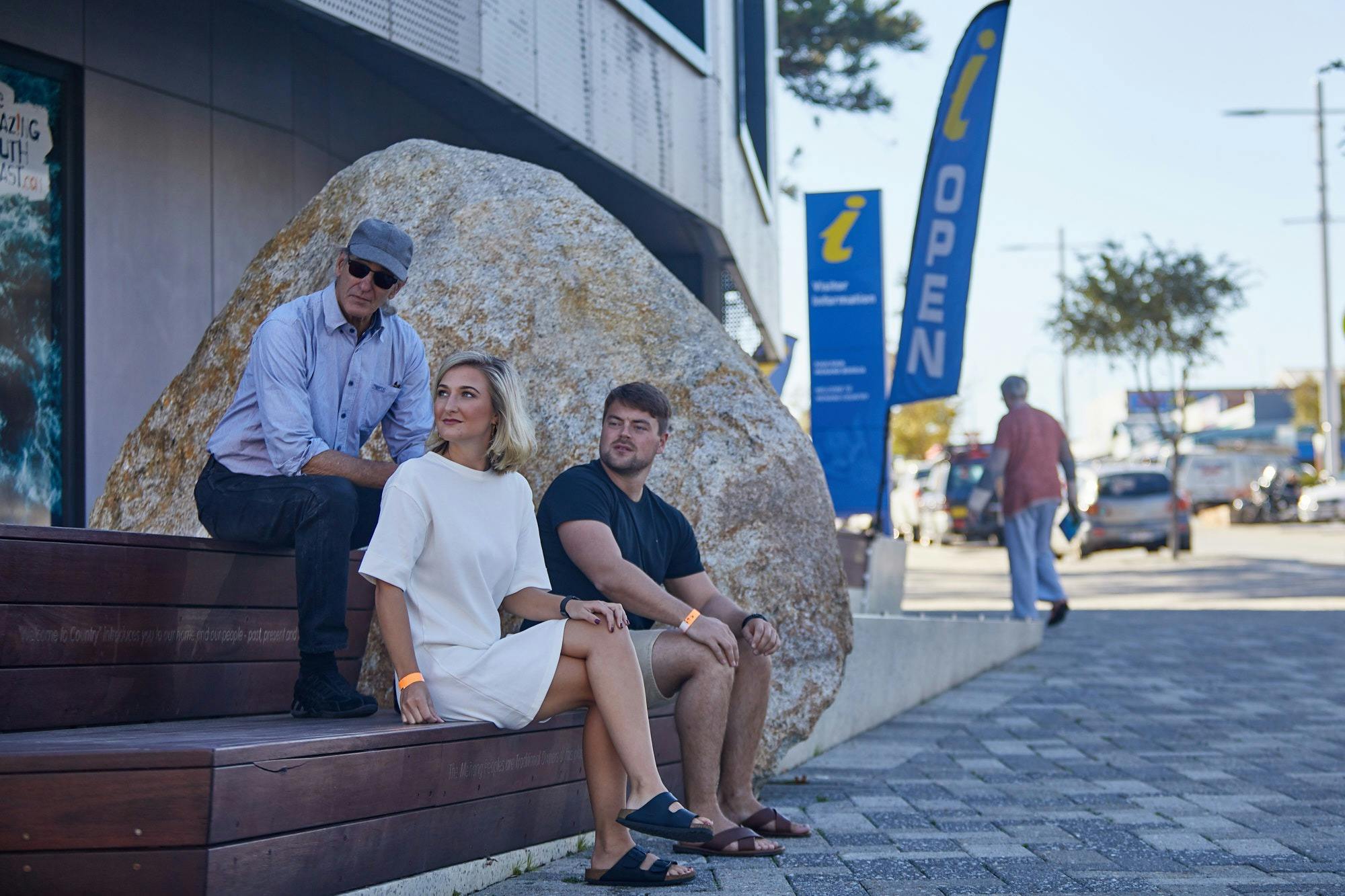 two men and woman sitting on granite steps with Information sign in background