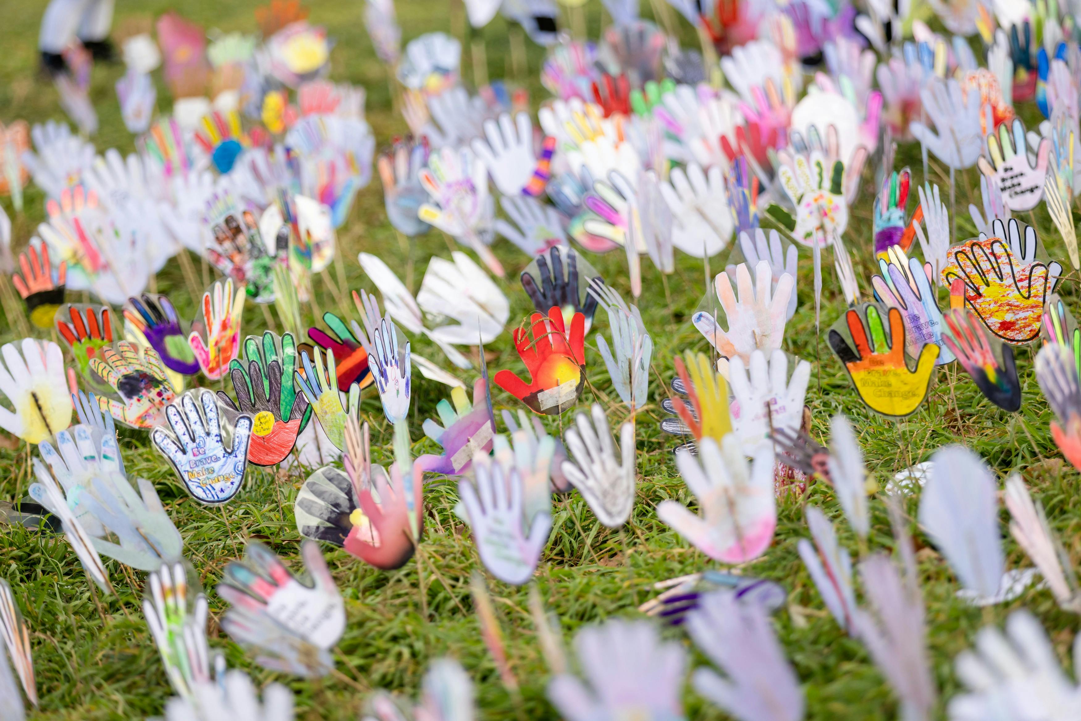 Colorful hand-shaped cutouts decorated with various patterns, mounted on sticks on grass area