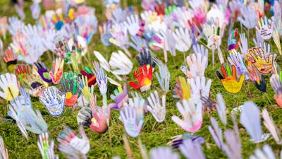 Colorful hand-shaped cutouts decorated with various patterns, mounted on sticks on grass area