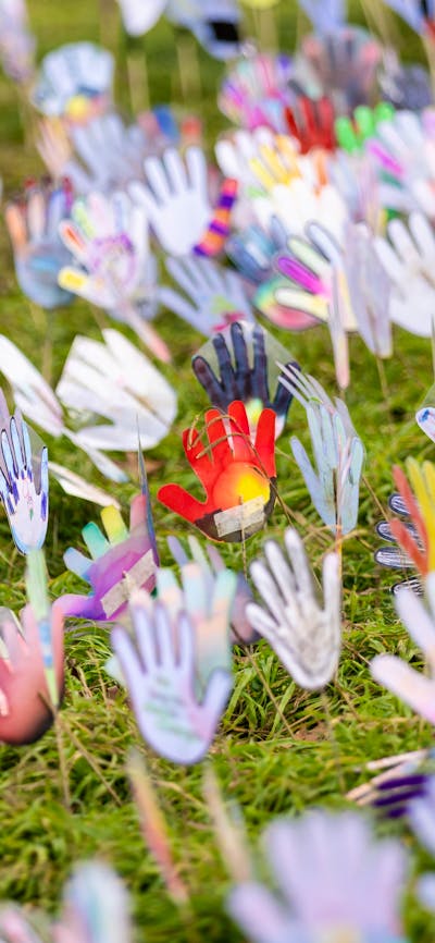 Colorful hand-shaped cutouts decorated with various patterns, mounted on sticks on grass area