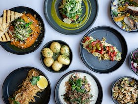 A spread of colourful dinner main meals and sides on dark plates on a white table cloth