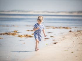 Child walking up the beach, barefoot and happy
