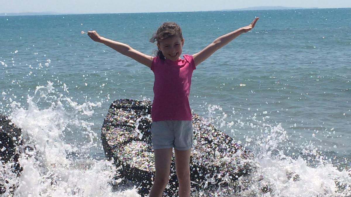 Girl on rocks with waves splashing in around her