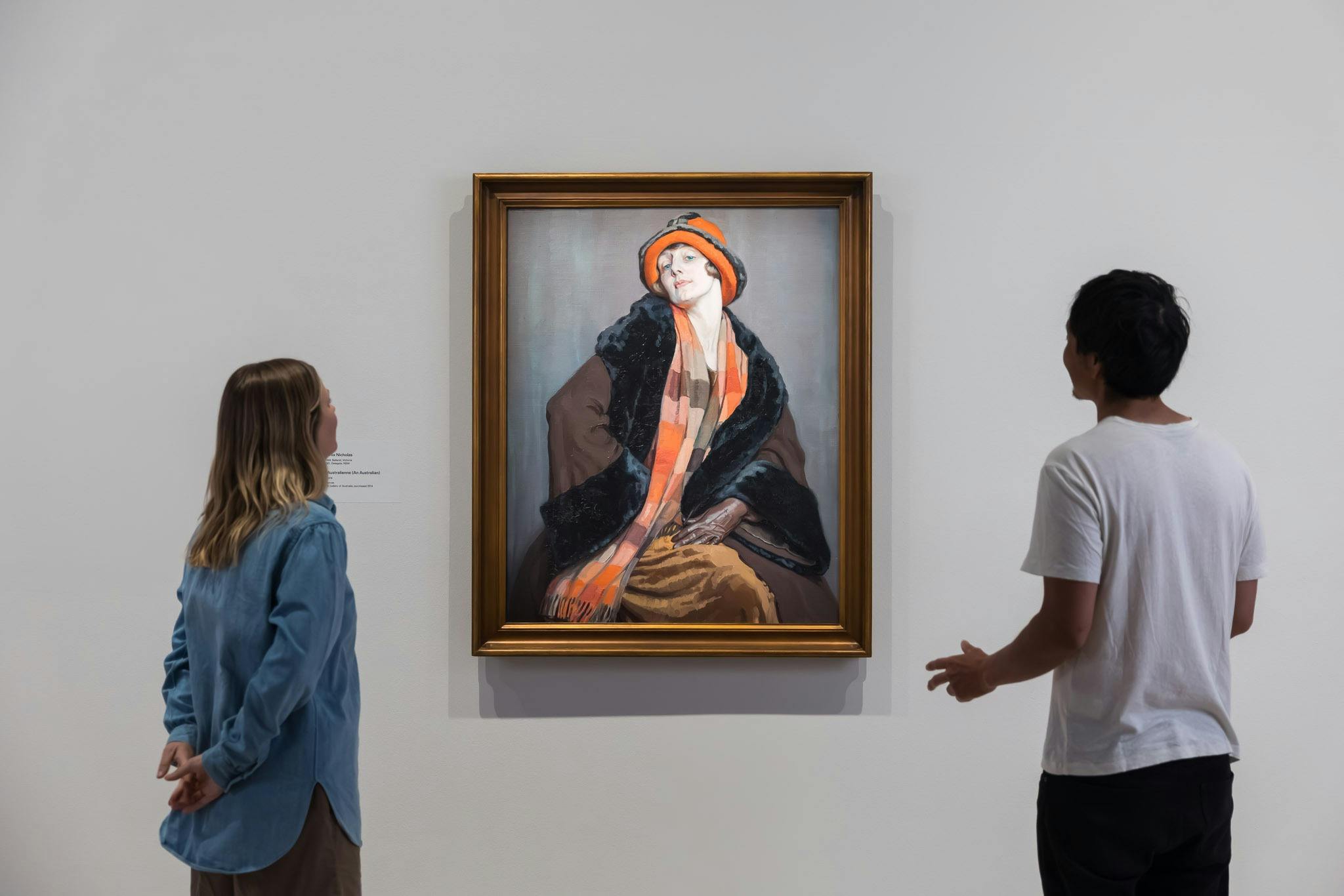 A young woman in a blue shirt and a young man in a white tee shirt admire a painting of a woman