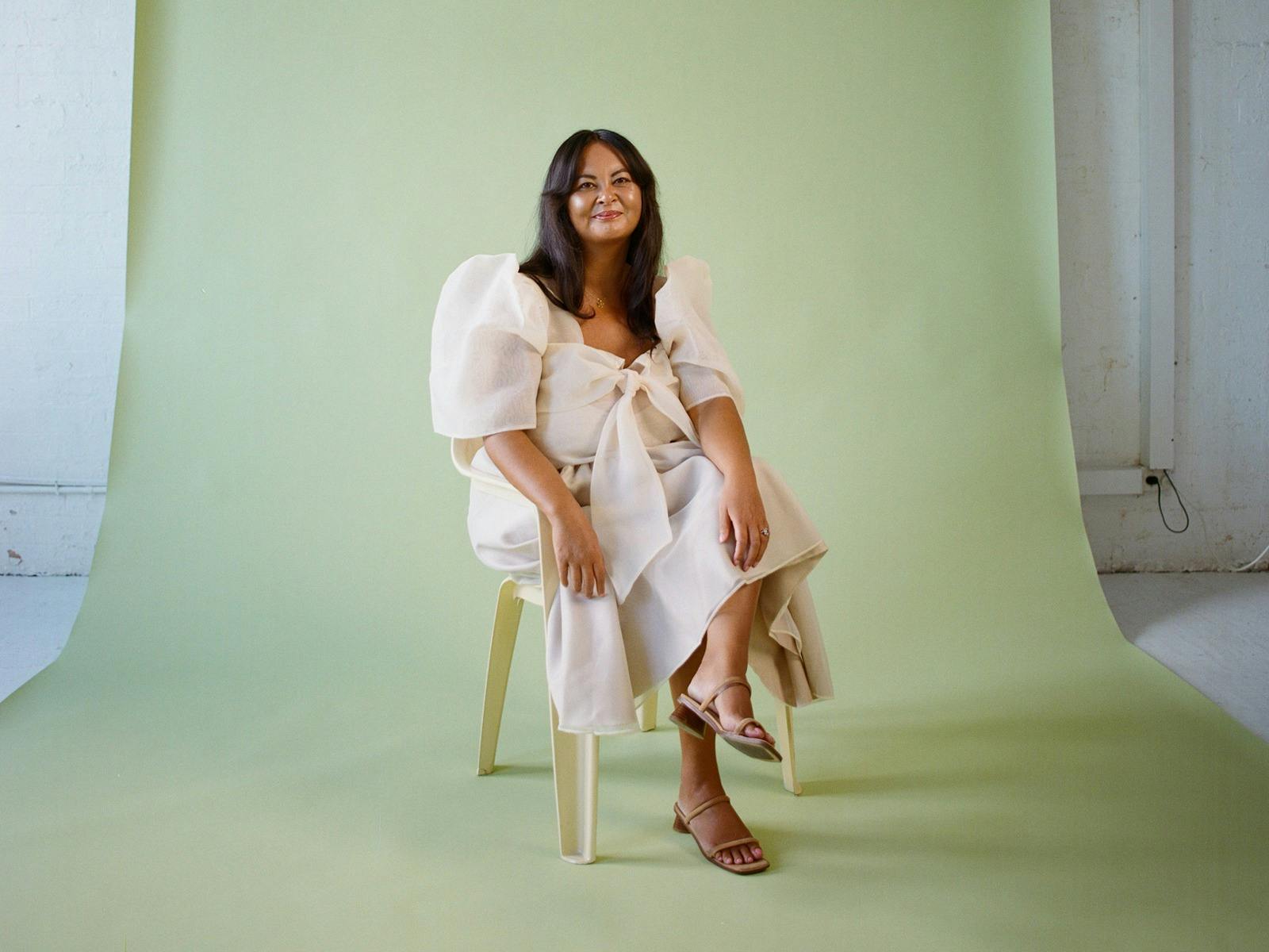 A woman sitting on a plastic chair, wearing traditional Filipiniana