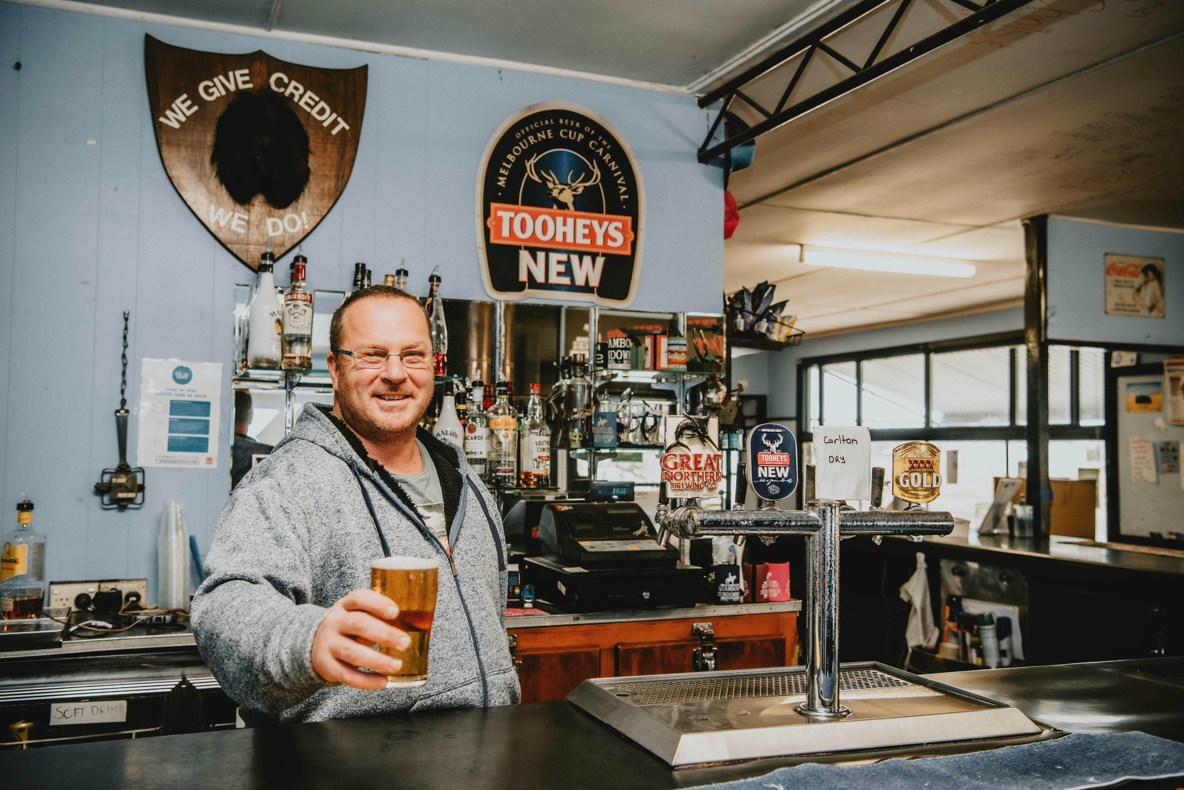 Man holding beer at bar with Tooheys New and Great Northern signs.