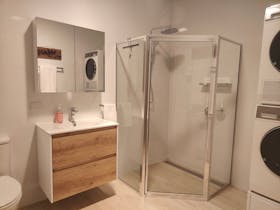 A picture of a tiled bathroom with a large shower, scandi style vanity, toilet, washer, dryer.