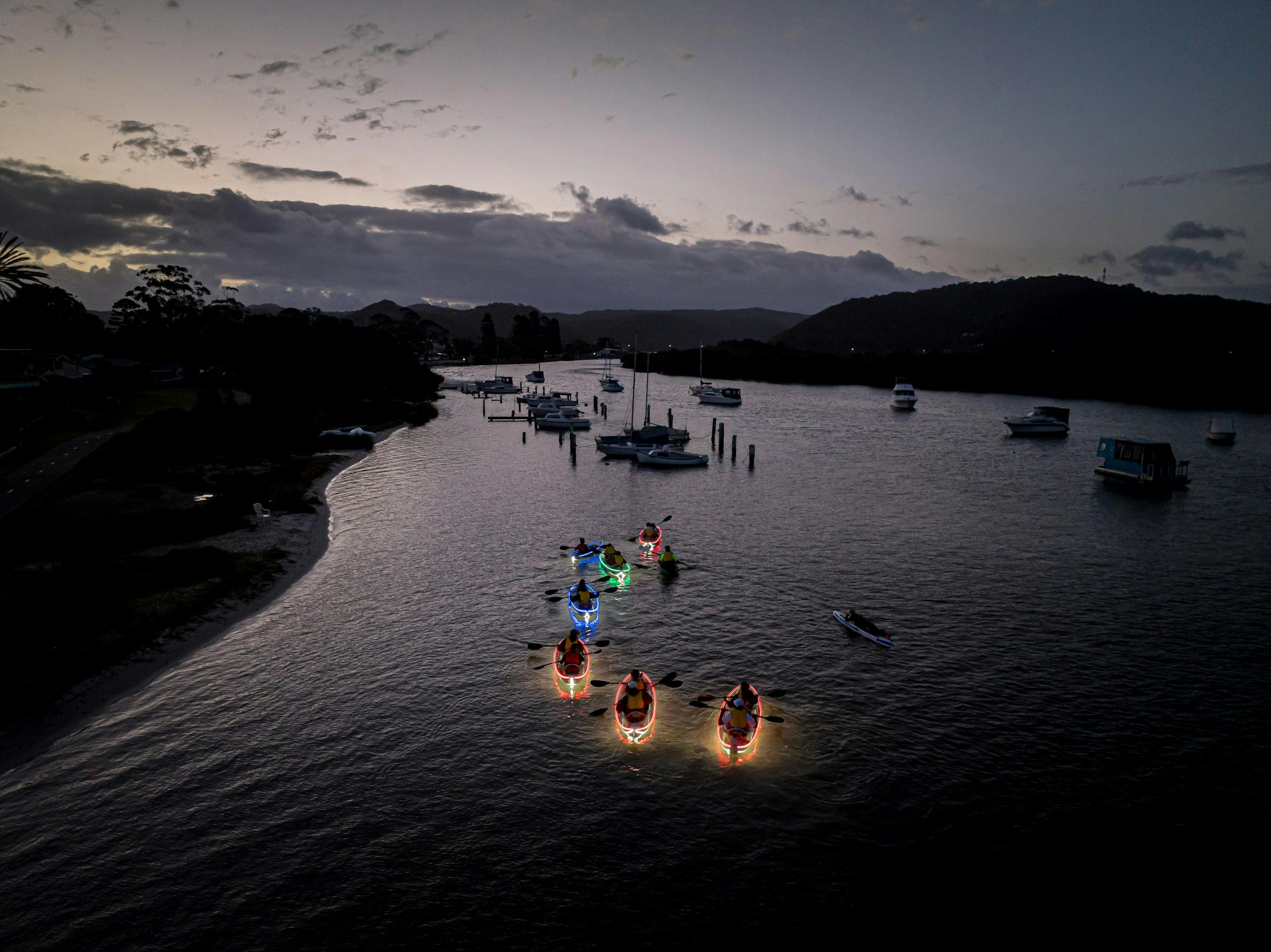 A drone photo of kyaks in the water with glow in the dark lights on them