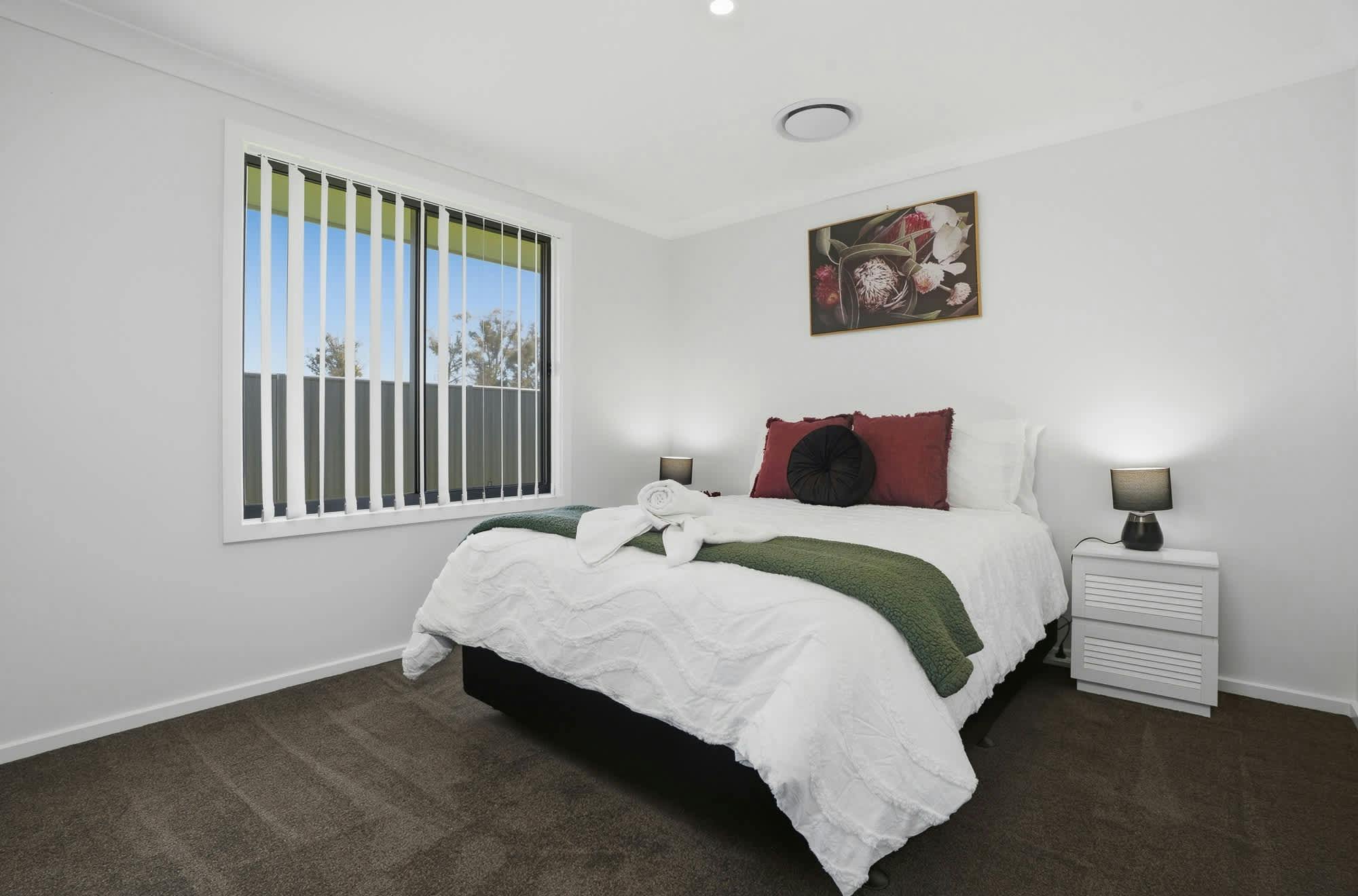 Bedroom with queen, bed side tables, lamp, white doona cover, cushions, throws and print