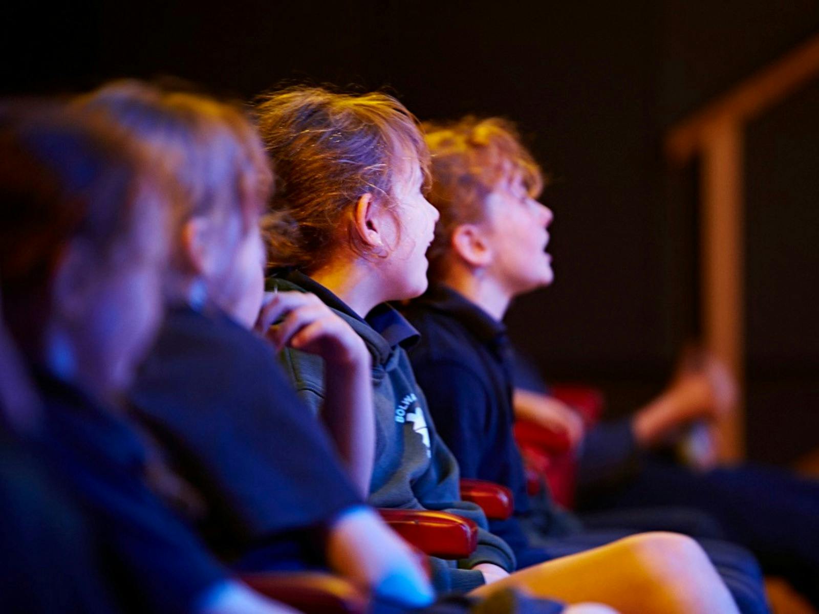 A group of children on a school excursion laughing at the show on stage (out of view)
