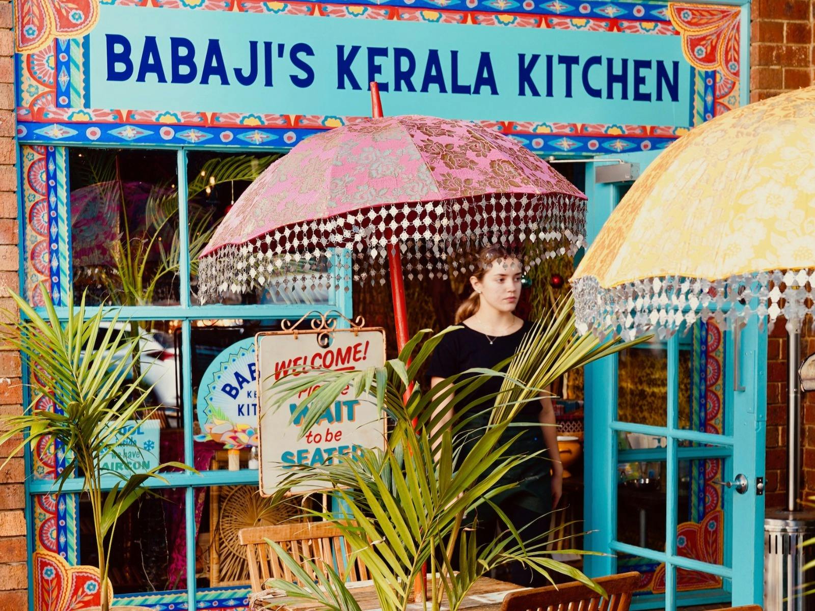 A colourful restaurant has its doors open to welcome everyone. Indian umbrellas decorate the space.